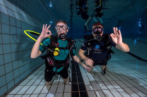 Twee duikers die het oke-signaal geven onder water in het zwembad