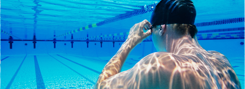 Man houdt zijn handen aan zijn zwembril en kijkt onderwater naar een leeg zwembad