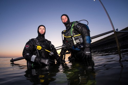 Twee duikers boven water staand in het buitenwater bij zonsondergang