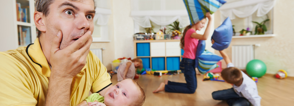 Vader met baby met op de achtergrond 2 kinderen die een kussengevecht hebben